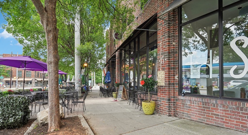 A storefront with a purple umbrella and a tree in front.